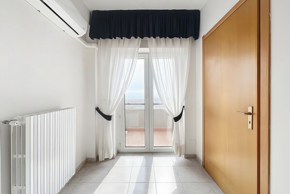 Un corridoio con termosifone, una porta scorrevole in vetro con tende e una porta in legno.
