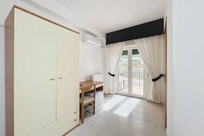 Ein Zimmer mit Kleiderschrank, Schreibtisch, Heizkörper und einer Glastür zum Außenbereich.