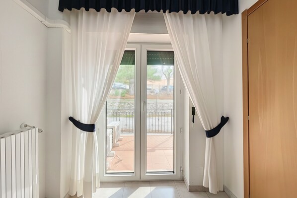 Ein Zimmer mit einer Glastür zum Außenbereich und einer Terrasse, mit weißen Wänden und einem Heizkörper.