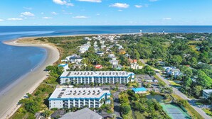 An aerial view of a coastal hotel with multiple buildings, a beach, and a lighthouse in the distance. - Fully equipped, 1 bedroom, 1 bath Bay front condo on Tybee Island with a pool (Tybee Island)