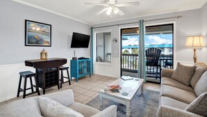 A living room with a sofa, coffee table, TV, and a balcony with a chair. - Fully equipped, 1 bedroom, 1 bath Bay front condo on Tybee Island with a pool (Tybee Island)