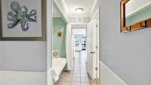 A hallway with a framed octopus artwork, a white door with a coat rack, and a view into a room with a bed and a window. - Fully equipped, 1 bedroom, 1 bath Bay front condo on Tybee Island with a pool (Tybee Island)