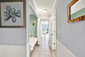 A hallway with a framed octopus artwork, a white door with a coat rack, and a view into a room with a bed and a window. - Fully equipped, 1 bedroom, 1 bath Bay front condo on Tybee Island with a pool (Tybee Island)