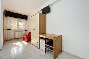 Una habitación con cama, escritorio, televisión instalada en la pared y ventana con cortinas.