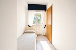 A small, well-lit bedroom with a single bed, a window with curtains, a radiator, and a wooden door. - B&B with Window - 232 - Santangelo - Pool (Monte Sant'Angelo)