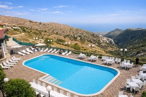 A swimming pool with lounge chairs and tables, surrounded by a stone deck, set against a mountainous backdrop. - B&B with Window - 232 - Santangelo - Pool (Monte Sant'Angelo)