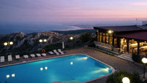 Une piscine avec des chaises longues, un bâtiment doté d’un toit rouge et une vue sur la côte.