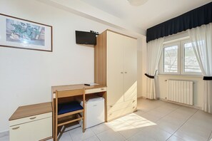 Ein Schlafzimmer mit Bett, Schreibtisch, Kleiderschrank, Heizkörper und einem Fenster mit Vorhängen.