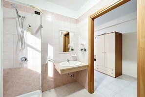 Ein Badezimmer mit Dusche, Waschbecken, Spiegel und Kleiderschrank.