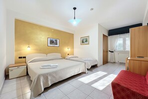 Ein Hotelzimmer mit zwei Betten, einem Holzschrank, einem roten Sessel und einem Fenster mit Vorhängen.