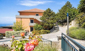 Ein mehrstöckiges Gebäude mit rotem Ziegeldach, einer Treppe zu einem Balkon und Blick auf das Meer.