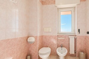 A bathroom with a toilet, bidet, and sink, a towel rack, and a window with a view. - Bright Sea View B&B with Balcony - 345 - Santangelo - Pool (Monte Sant'Angelo)