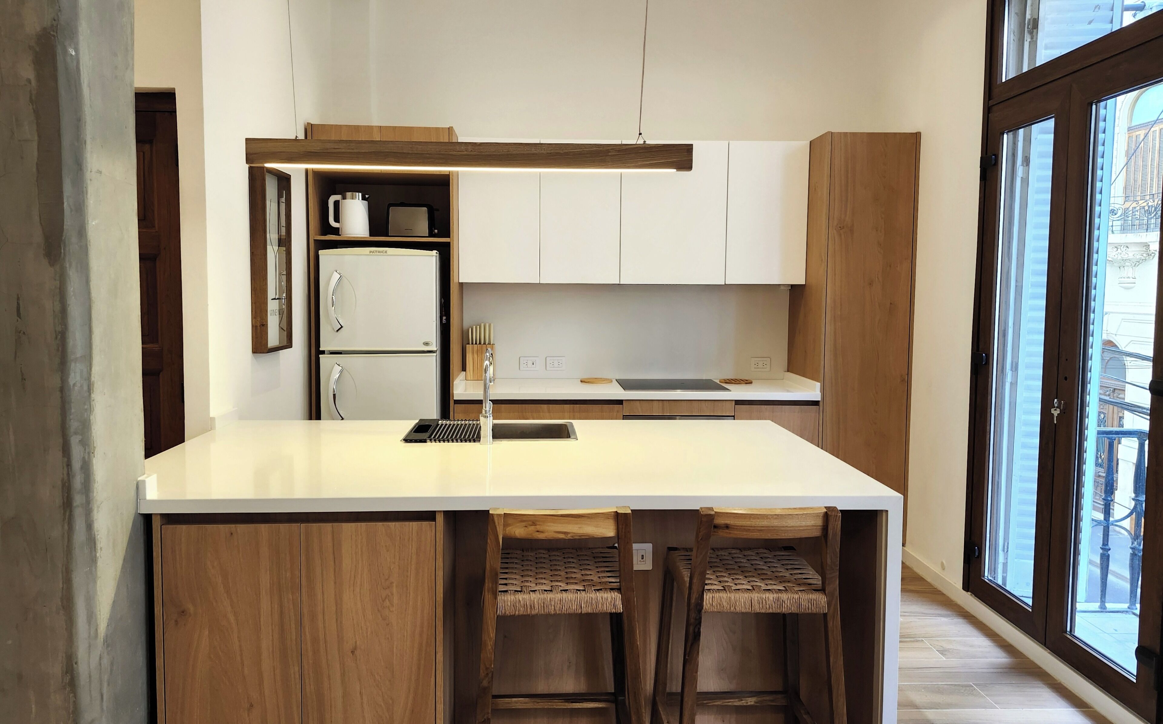 A modern kitchen with a central island, wooden cabinets, and a view of the city through large windows.