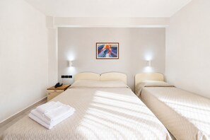 Quarto de hotel com duas camas, uma mesinha de cabeceira, um quadro na parede e duas luminárias fixadas na parede.