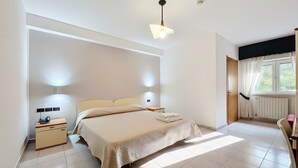 A bedroom with a bed, bedside lamps, a nightstand, a window with curtains, and a radiator. - B&B with Window - 351 - Santangelo - Pool (Monte Sant'Angelo)