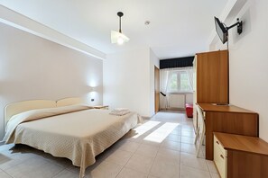 Ein Schlafzimmer mit Bett, Nachttischlampe, Holzschreibtisch und einem Fenster mit Vorhängen.