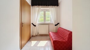 A room with a wooden door, a window with white curtains, a radiator, and a red sofa. - B&B with Window - 351 - Santangelo - Pool (Monte Sant'Angelo)