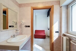 Ein Badezimmer mit Waschbecken, zwei Haartrocknern, einem Spiegel und einer roten Bank im Hintergrund.