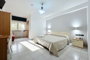 Ein Schlafzimmer mit Bett, Nachttischen, Schreibtisch, Stuhl und einem Fenster mit Vorhängen.