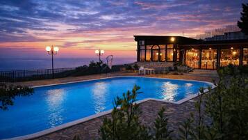 Una piscina con piastrelle di pietra, un edificio con ampie finestre e un cielo al tramonto.
