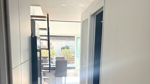 A narrow hallway with a door on the left, a trash bin on the right, and a view of a patio area with outdoor furniture. - Naturiste Cap d'Agde Villa Héliovillage 90 (Agde)