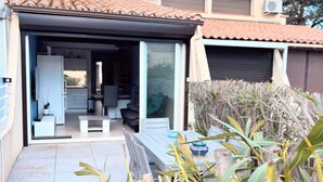 A modern house with a covered patio, a visible kitchen area, and a garden with plants. - Naturiste Cap d'Agde Villa Héliovillage 90 (Agde)