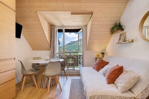 Et hyggeligt værelse med spiseplads, en seng med puder, en balkon med udsigt over bjergene og træpaneler.