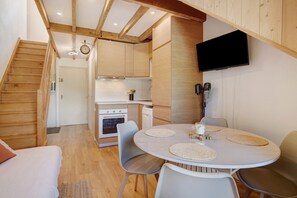 A modern kitchen with wooden beams, a dining area with a round table, and a TV mounted on the wall. - Duplex for 6, 30m from the Ski Lifts (Les Deux Alpes)