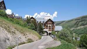Un complejo turístico de montaña con un camino serpenteante, un gran edificio con balcones y un cielo azul despejado.
