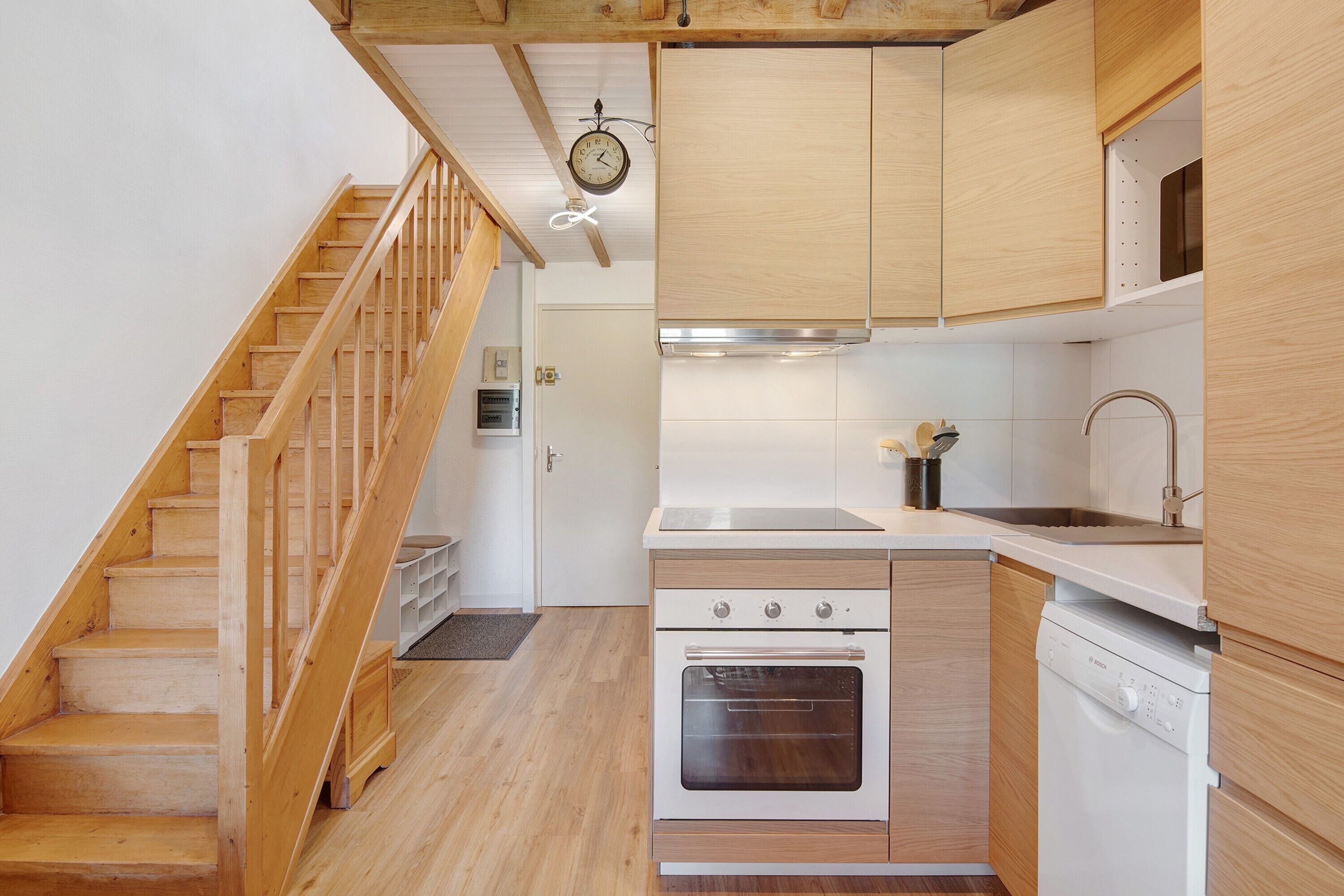 A kitchen with wooden cabinets, a built-in oven, a dishwasher, and a wooden staircase.