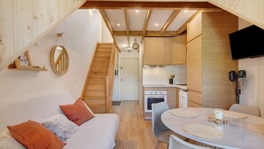 Un ambiente acogedor con sofá, una mesa de comedor con individuales, una zona de cocina con armarios de madera y una escalera.