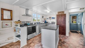 Una cocina con gabinetes blancos, una isla central, una estufa y un cartel que dice 'APPLES'.