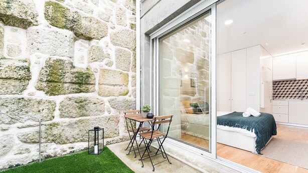 Una habitación moderna con pared de piedra, puerta de vidrio que da a una cocina y un pequeño espacio al aire libre con mesa y sillas.