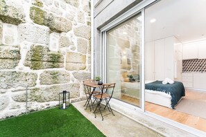 A modern room with a stone wall, a glass door leading to a kitchen, and a small outdoor seating area with a table and chairs. - GuestReady - Studio in Porto (Porto)