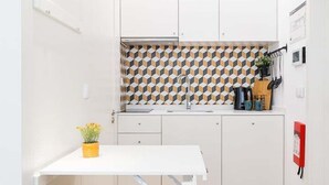 Una cocina compacta con armarios blancos, un salpicadero estampado, una pequeña mesa de comedor con taburetes y un extintor de incendios en la pared.