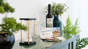 Una mesa de vidrio con una botella de vino, copas de vino, un cartel con un código QR y una tarjeta de bienvenida.