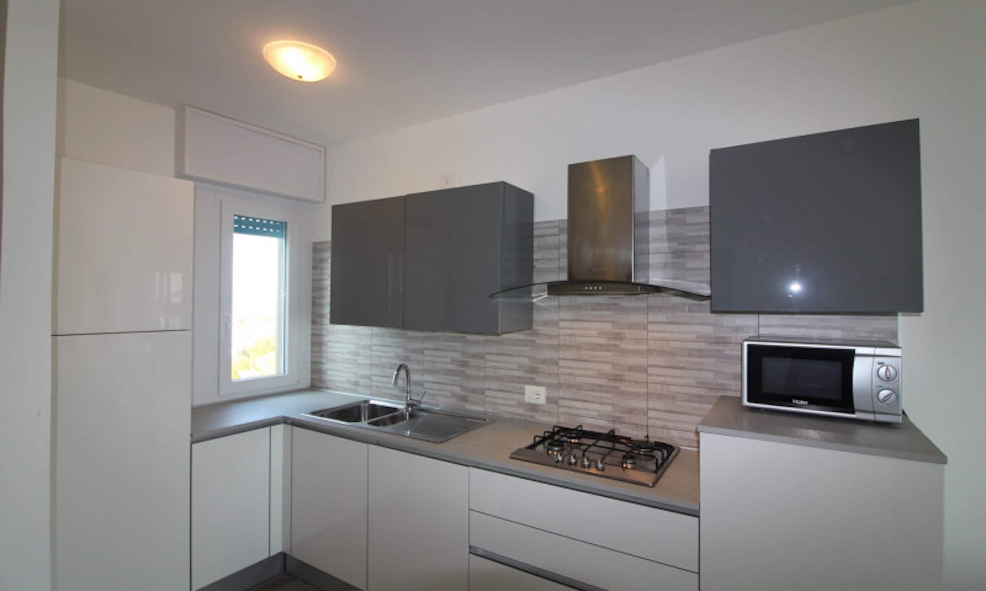 A modern kitchen with white cabinets, a stainless steel sink, a gas stove, and a microwave.