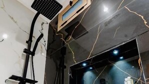 A modern bathroom with a marble wall, a black marble vanity, a mirror, and a shower with a handheld showerhead. - Hotel Rhali Dakhla (Dakhla)