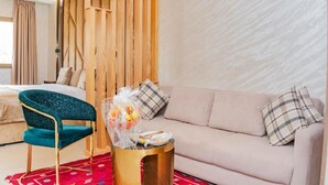 A hotel room with a bed, a teal chair, a sofa, and a small table with a fruit basket. - Hotel Rhali Dakhla (Dakhla)