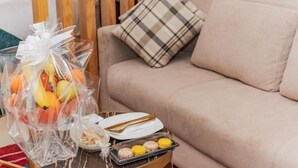 A living room with a beige sofa, a plaid pillow, a small table with a fruit bouquet, a plate with a fork, and a tray with macarons. - Hotel Rhali Dakhla (Dakhla)