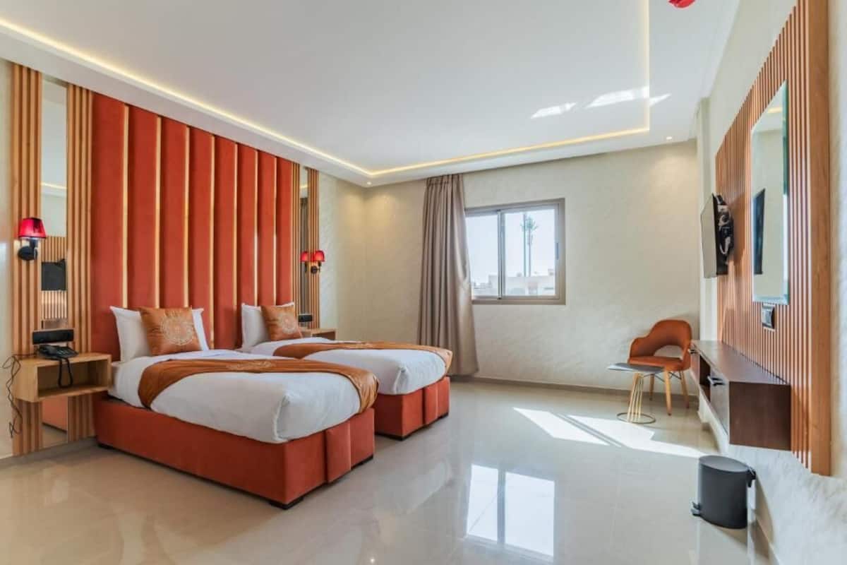 A modern hotel room with two beds, a desk, a chair, a TV, and a window.