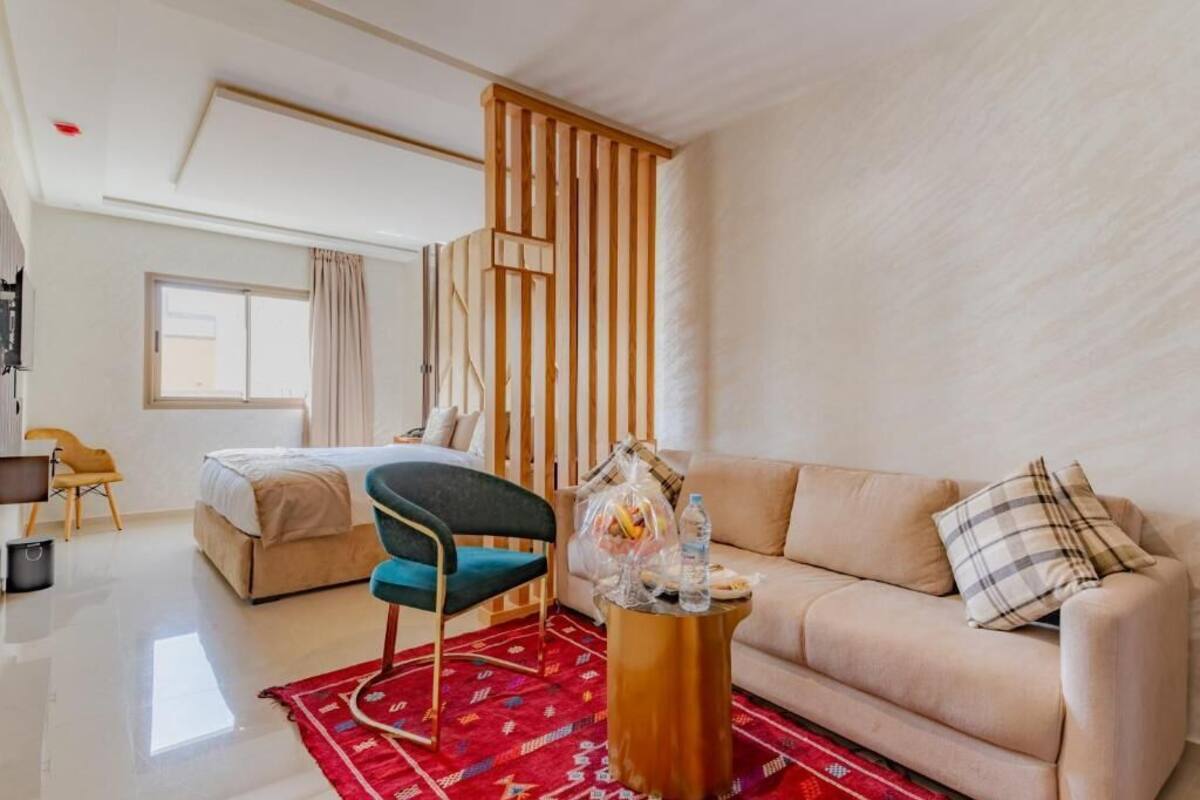 A modern hotel room with a bed, a sofa, a chair, and a small table with a red rug.