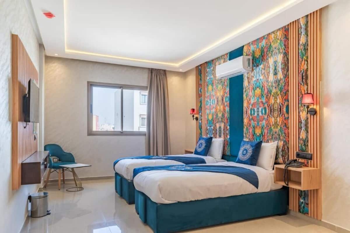 A modern hotel room with two beds, a desk, and a chair.