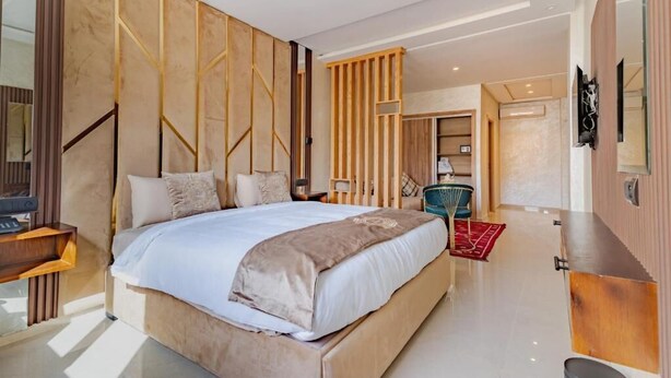 A modern bedroom with a large bed, wooden paneling, a desk, and a TV mounted on the wall. - Hotel Rhali Dakhla (Dakhla)