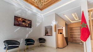 A reception area with a modern design, featuring a reception desk, three chairs, a flag, and a painting on the wall. - Hotel Rhali Dakhla (Dakhla)