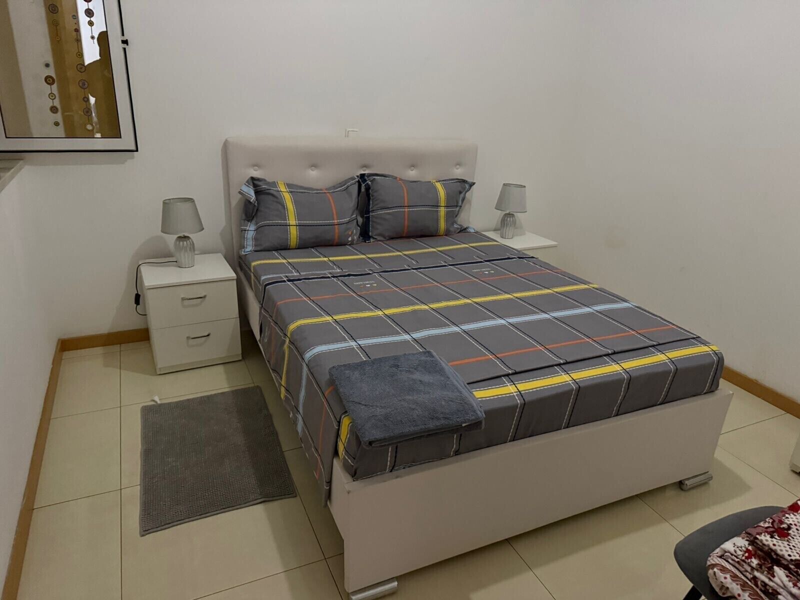 Une chambre à coucher bien rangée, avec un lit, deux tables de chevet, une commode, un tapis et une chaise.