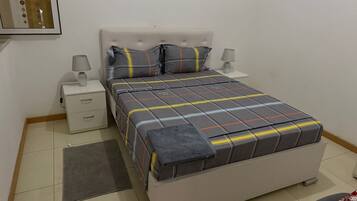 Une chambre à coucher bien rangée, avec un lit, deux tables de chevet, une commode, un tapis et une chaise.