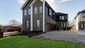 Une maison moderne à deux étages, dotée d’une façade en pierre, de grandes fenêtres et d’un garage.