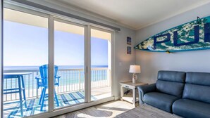 A room with a large sliding glass door leading to a balcony with a view of the ocean. There is a blue sofa and a small table with a lamp. - Seychelles 407 (Panama City Beach)