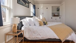 A bedroom with a bed, bedside table, lamp, and a painting on the wall.